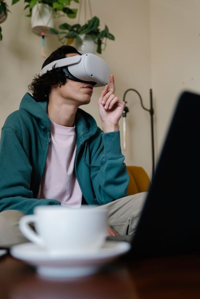 Low angle of engaged male pointing up while experiencing virtual reality in headset at table with laptop